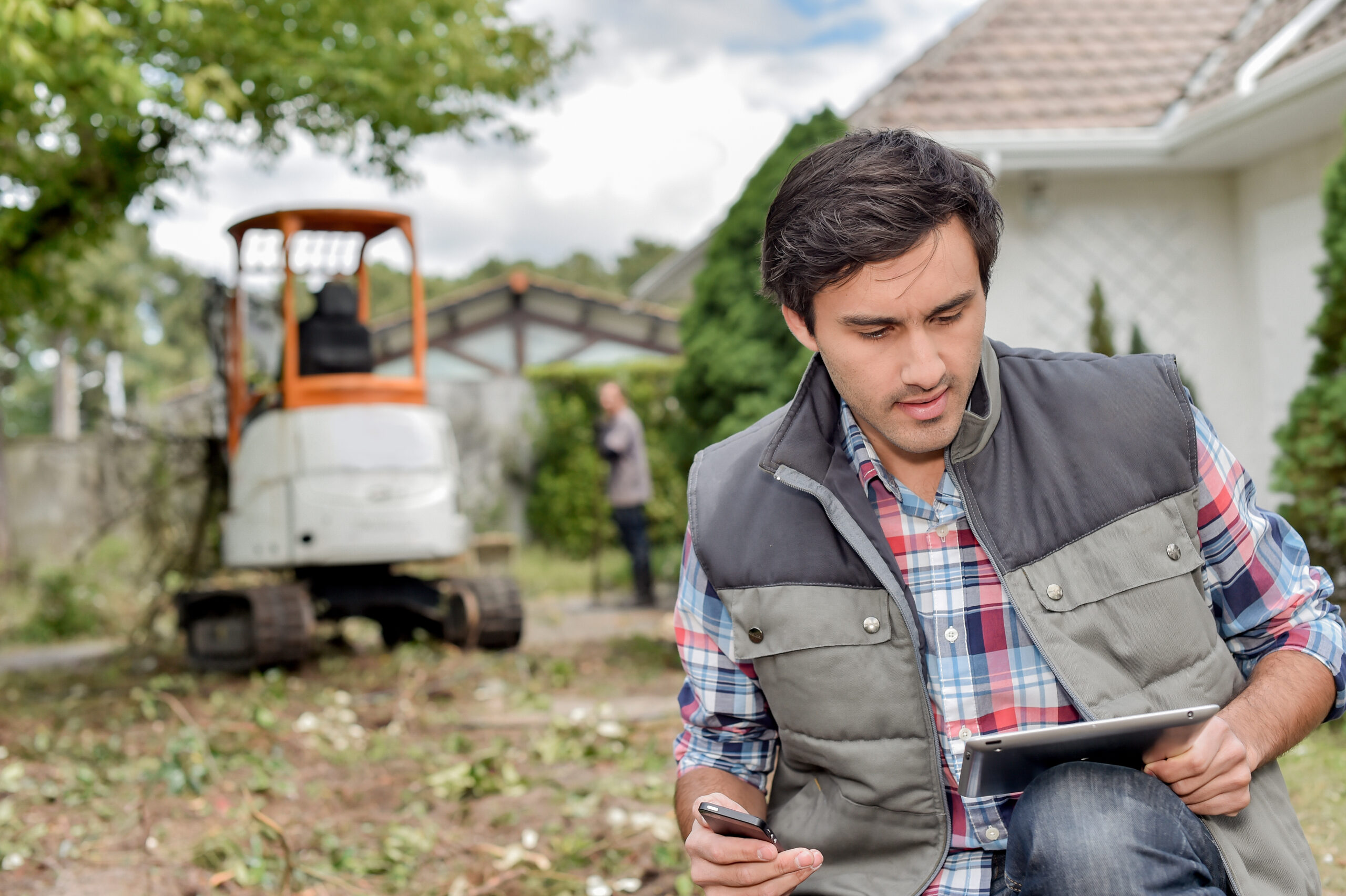 Man outside using tablet, digger in background